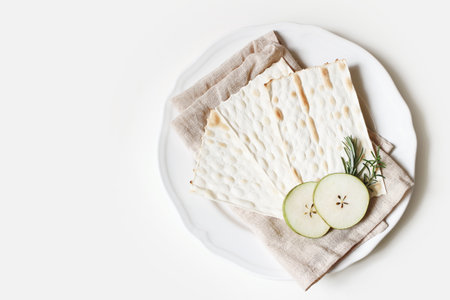 Kosher food concept. Seder dinner composition. Matzo bread, egg, apple fruit and herbs on porcelain plate and linen napkin. Happy passover greeting card, invitation. Flat lay, top view.の写真素材
