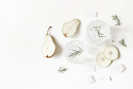 Cold pear cocktails, alcohol drinks in two glasses with soda, fruit slices, ice cubes and rosemary herbs leaves isolated on white table background. Summer refreshment concept. Flat lay, top view.の写真素材