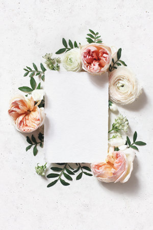 Feminine wedding, birthday mock-up scene. Blank paper greeting card. Floral frame of blush pink English roses, ranunculus flowers and lentisk leaves. Concrete table background. Flat lay, top view.の写真素材