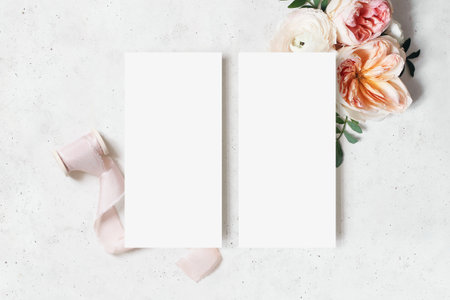 Wedding, birthday stationery mock-up scene. Blank menu cards. Decorative floral corner. Green leaves, pink English roses, ranunculus flowers and ribbon. Concrete table background. Flat lay, top viewの写真素材