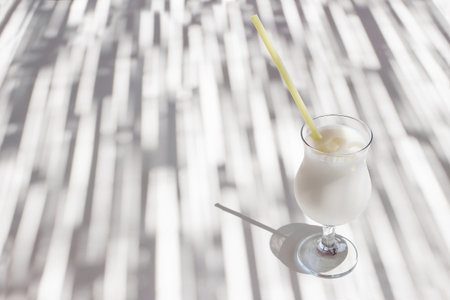 Pina colada cocktail with yellow drinking straw, coconut milk and ice cubes on white bar table....