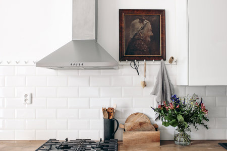 Modern eclectic kitchen interior. White brick wall with metro tiles, peg rails and oil painting. Wooden countertop, stainless steel hood and gas stove. Scandinavian design. Home staging, concept.の写真素材