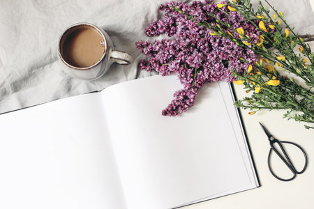 Styled spring breakfast scene, feminine floral composition. Bouquet of purple lilac branches, yellow broom Cytisus, cup of coffee, linen tablecloth isolated on white table background. Flat lay, top.の写真素材
