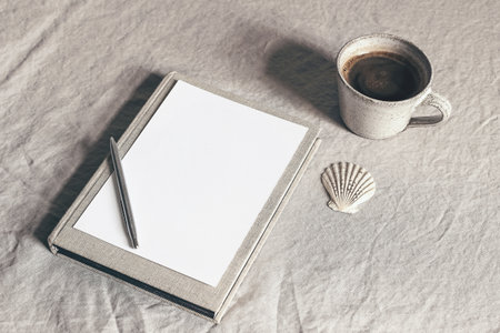 Cup of coffee, book, blank sheet of paper and silver pen. Moody breakfast table stationery mockup...