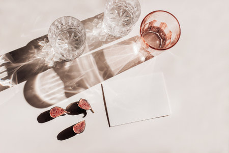 Summer stationery still life scene. Glasses of water, cut figs fruit. Pink table background in sunlight. Blank business, greeting card, invitation mockup scene. Long harsh shadows. Flat lay, top viewの写真素材