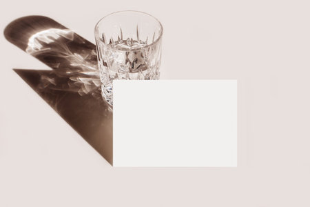 Modern summer stationery still life. Glass of water, cocktail with long shadow. Blank business card mock up scene. Beige table background in sunlight. Flat lay, high angle view. Empty copyspace.の写真素材