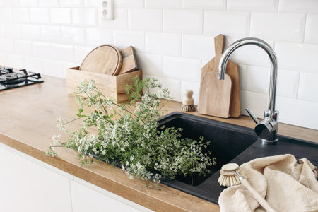 Closeup of kitchen interior. White brick wall, metro tiles, wooden countertops with chopping boards. Cow parsley plants in black sink. Modern scandinavian design. Home staging, cleaning concept.の写真素材