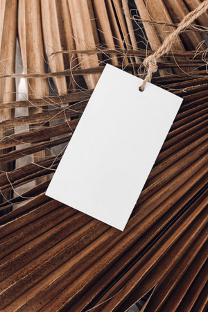 Closeup of blank gift, product tag mock-up with natural rope on dry palm leaves. Empty paper label. Tropical still life composition. Branding, summer sale concept. Flat lay, top view., verticalの写真素材