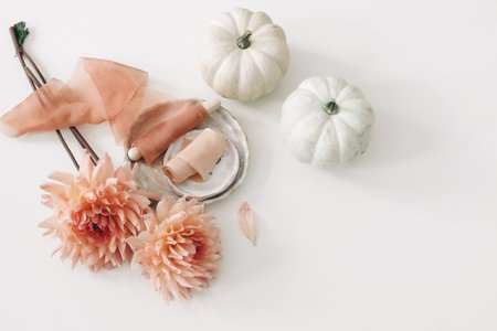 Autumn floral wedding composition, feminine still life. Pink dahlia flowers, silk ribbons and white pumpkins isolated on table background. Fall, Thanksgiving design. Flat lay, top view. Garden crop.の写真素材