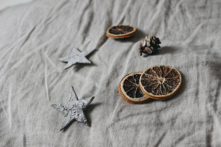Christmas neutral still life composition. Birch bark stars, larch cones and dry orange slices on grey linen table cloth background. Moody winter design. Selective focus.の写真素材