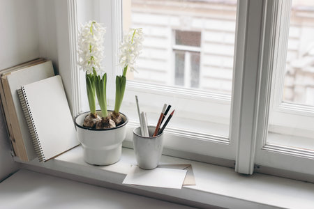 Easter spring still life. Greeting card, books and diary on window sill. White hyacinth in flower pot. Blank greeting card mockup. Pencils in ceramic holder. Home office concept. Scandinavian interiorの写真素材