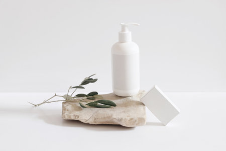 Set of cosmetic products on light background. White plastic pump bottle for shampoo, lotion mockup on stone podium. Blank soap box. Green live tree branch. Healthy cosmetology, spa treatment concept.の写真素材
