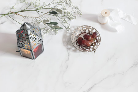 Vintage Moroccan, Arabic lantern. Olive tree branch, gypsophila flowers and grapes on silver plate. White marble table background. Muslim holiday Ramadan Kareem. Empty space, flat lay, top view.の写真素材