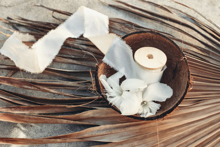 Summer tropical lifestyle scene. Oleander blossoms and white silk ribbons spools in coconut shell....