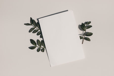 Summer wedding stationery mock-up. Blank greeting card, invitation and dark green lentisk leaves on beige table background in sunlight. Natural light and shadow overlay. Flat lay, top view.の写真素材
