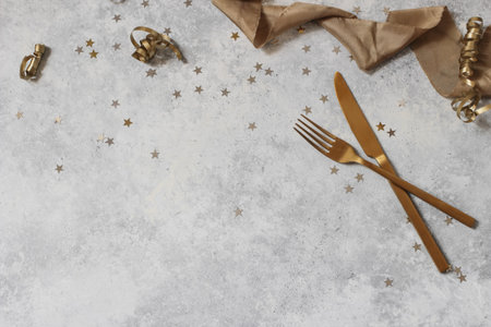 New Year still life composition with golden confetti stars, table knife, fork and silk ribbons. Party decoration, celebration concept. Flat lay, top view. Empty copy space. Grunge table background.の写真素材