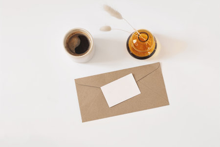 Stationery still life. Empty paper business card and envelope mockup. Cup of coffee in mug. Dry lagurus grass in glass vase on white table background. Flat lay, top overhead view. Branding identity.の写真素材