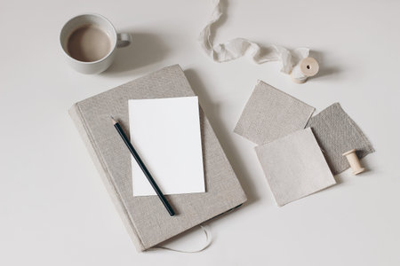 Craft still life. Beige fabric linen swatches and silk ribbon isolated on beige table background. Cup of coffee. Blank greeting card mockup, pencil on old book, diary. Mood board project flat lay, topの写真素材