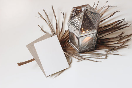 urning silver Moroccan, Arabic lantern with dry palm leaf isolated on white table. Blank greeting card mockupfor Muslim holiday Ramadan Kareem or boho wedding. Festive background.Flat lay, top view.の写真素材