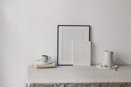 Easter home spring still life. Blank picture frames mockups. Cup of coffee, books on linen table cloth. White ceramic jug and quail eggs. Home office concept. Scandinavian interior.の写真素材