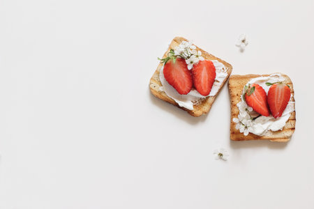Two roasted bread sandwiches with cottage cheese and strawberries isolated on white table background. Toasts with fresh fruit and blossoms. Healthy breakfast, morning meal. Flat lay, top view.の写真素材