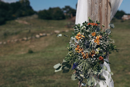 Floral decorative decoration of the white wooden wedding arch with fresh flowers. Holding a farm, boho wedding ceremony in the open air. Summer outdoor party, blue sky, green lawn. Blurred background.の写真素材
