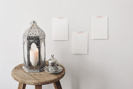 Silver Moroccan, Arabic lantern with cup of Turkish tea, coffee drink on old wooden stool. Blank greeting card mockups taped on white wall. Muslim holiday Ramadan Kareem. Festive background.の写真素材