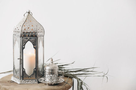 Ramadan still life. Closeup of silver Moroccan, Arabic lantern. Cup of Turkish tea, coffee. Dry palm leaf on old wooden stool. Blurred background, selective focus. Muslim festive holiday background.の写真素材