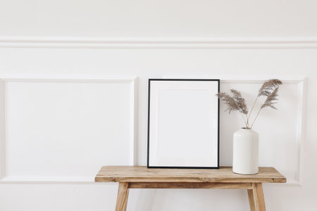 Summer, fall still life photo. Vase with dry reed, grass on old wooden bench. Blank black picture frame mockup. White wall moulding background, stucco decor. Empty copy space. Elegant interior.の写真素材