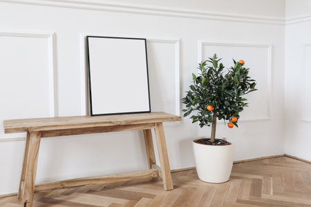 Elegant mockup scene. Tangerine, citrus calamondin fruit tree in flower pot. Blank black picture frame on old wooden bench, table. Wall moulding background, trim. Summer living room decor.の写真素材