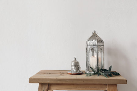 Ramadan Kareem still life. Ornamental lantern with burning candle and Turkish silver cup with tea or coffee. Green olive tree branches on old wooden table background. Muslim Iftar dinner. No peopleの写真素材