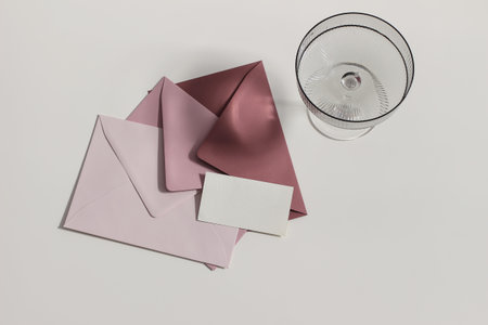 Wedding stationery still life. Champagne, cocktail glass, long shadows. Blush pink , crimson envelopes. Blank business card mock up. Soft beige table background in sunlight. Flat lay, top view.の写真素材