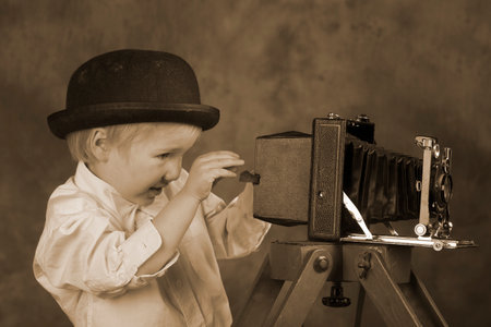 Young blond boy holding retro camera with bellows in photo studio, photographer, vintage sepia toneの写真素材