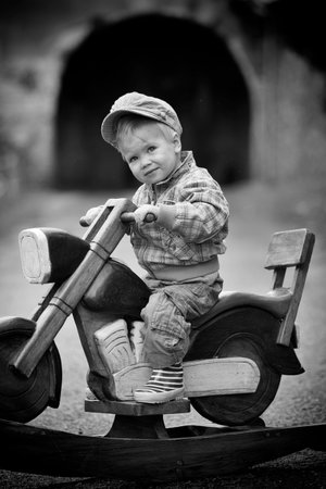 Young boy and a wooden rocking motorbike on the street, retro styleの写真素材