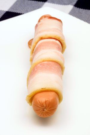 raw hot dog rapped in bacon o white plate の写真素材