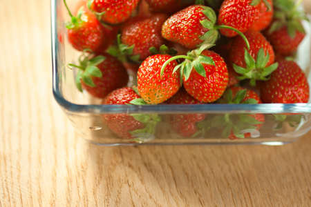 Strawberry fruit in a glass container on a wooden surface. Bokeh blurred image.の写真素材