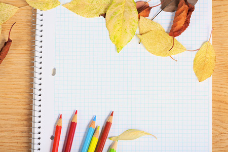 Notebook with colored pencils and autumn leaves on a wooden surface.の写真素材