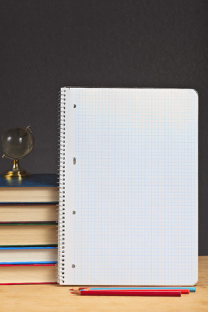 Notebook with colored pencils and pile of books on a wooden surface.の写真素材