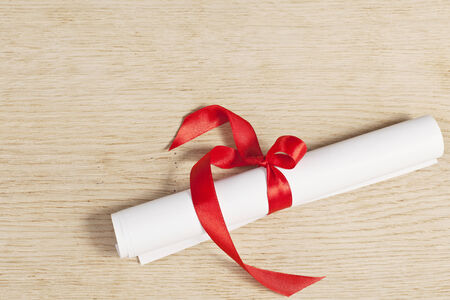Scroll of paper with a red ribbon on a wooden surface.の写真素材