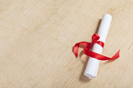 Scroll of paper with a red ribbon on a wooden surface.の写真素材