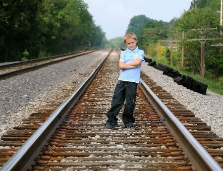 A cute young boy stands on railroad tracks to pose for a photograph.の写真素材