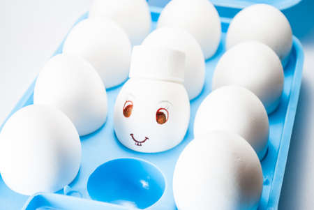 Egg with a smile and bunny teeth and a white cap in a blue egg trayの写真素材