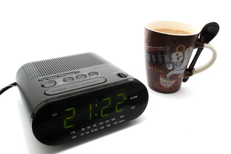 A Clock alarm radio and a cup full of coffeeon isolated white backgroundの写真素材