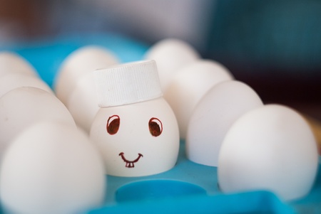 Egg with a smile and bunny teeth and cap in a blue egg trayの写真素材