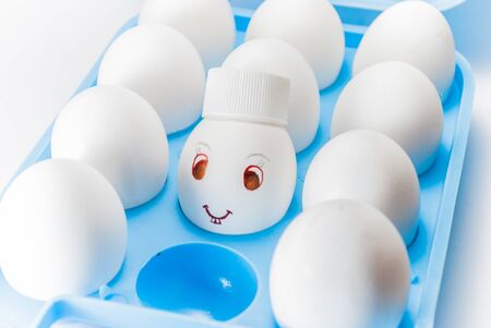 Egg with a smile and bunny teeth and a cap in a blue egg trayの写真素材