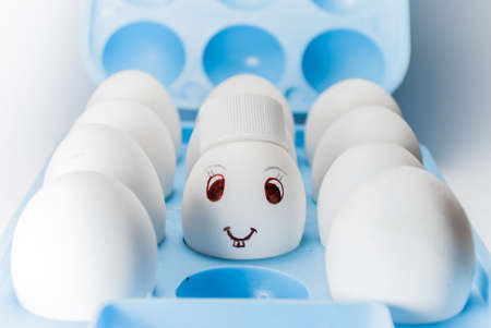 Egg with a smile and bunny teeth and a cap in a blue egg trayの写真素材