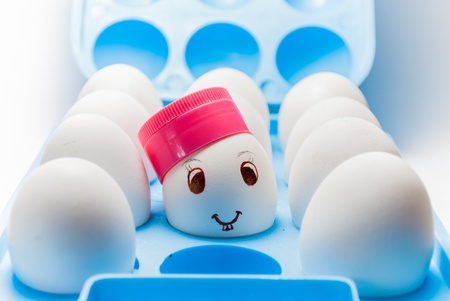 Egg with a smile and bunny teeth and a cap in a blue egg trayの写真素材