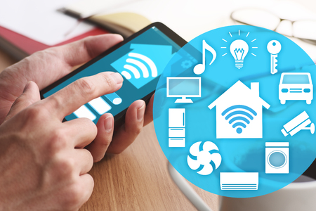 Smart home and IOT concept. Smartphone and many icons. Closeup of male hands touching smartphone screen for using smart home app at table.の写真素材