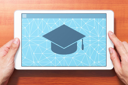 E-learning concept image. Closeup of hands touching white tablet computer on wooden desk. Application on screen. Front view image.の写真素材