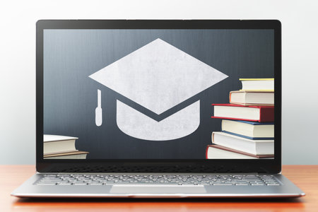 E-learning concept image. Laptop computer on wooden desk.  Book, bachelor's cap icon and blackboard. Front view image.の写真素材